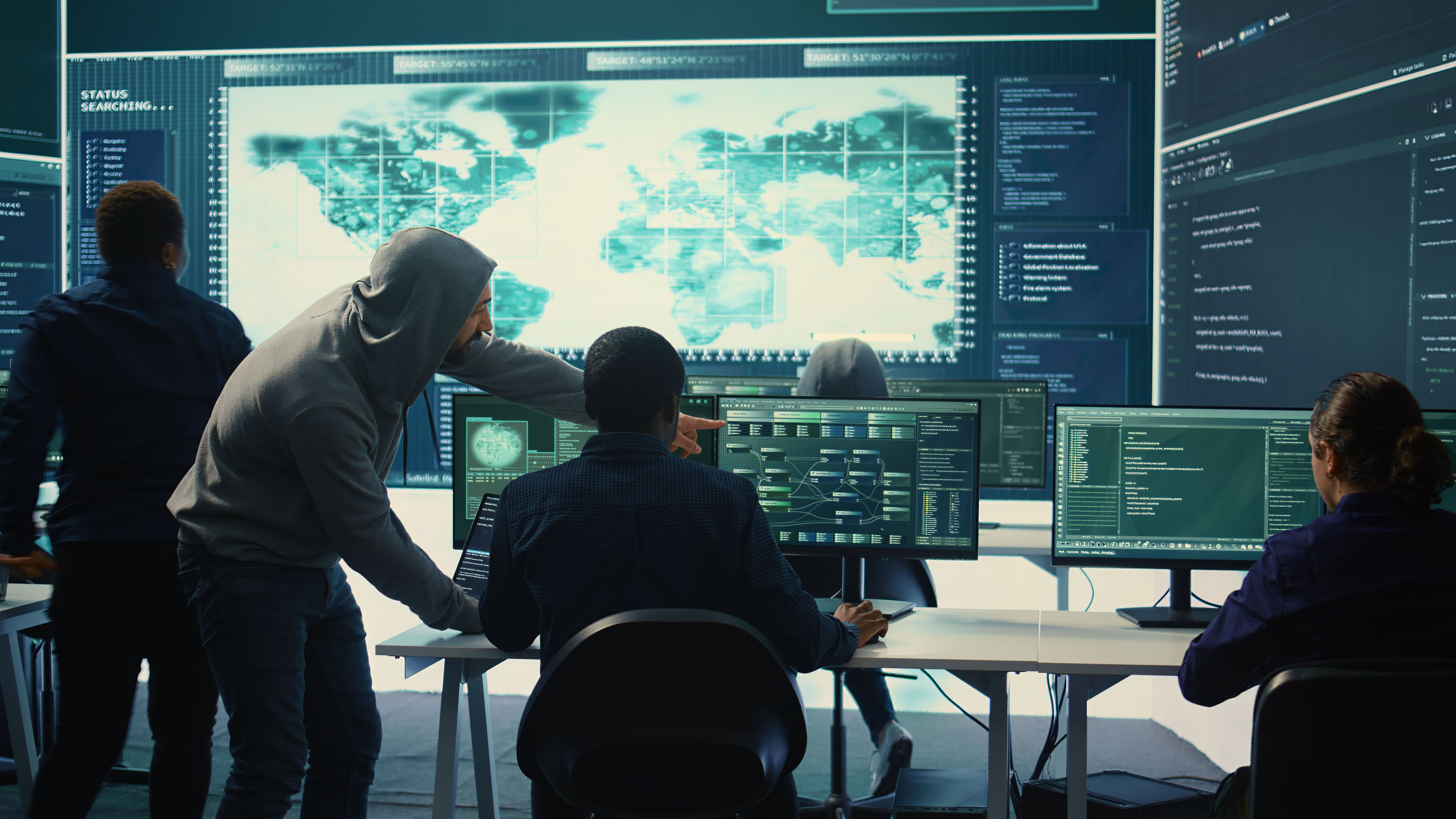 Security analysts monitoring a large world map display and data dashboards in a control room, conducting a security controls review