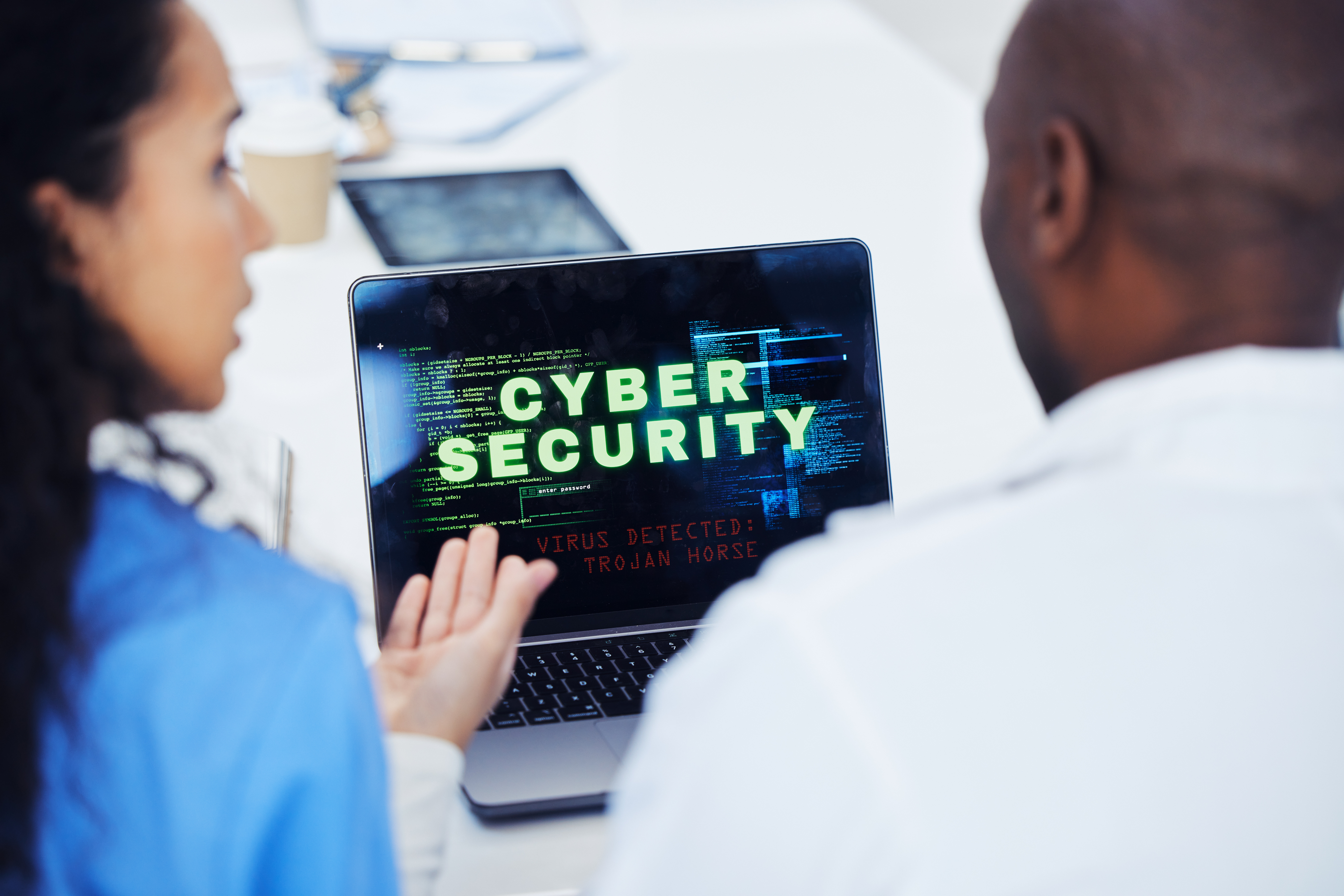 Two colleagues are viewing a laptop screen showing a Trojan horse virus alert, prompting an urgent cyber risk assessment